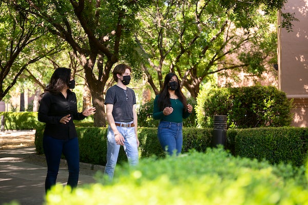 Three ASU students walk while social distancing and wearing masks.