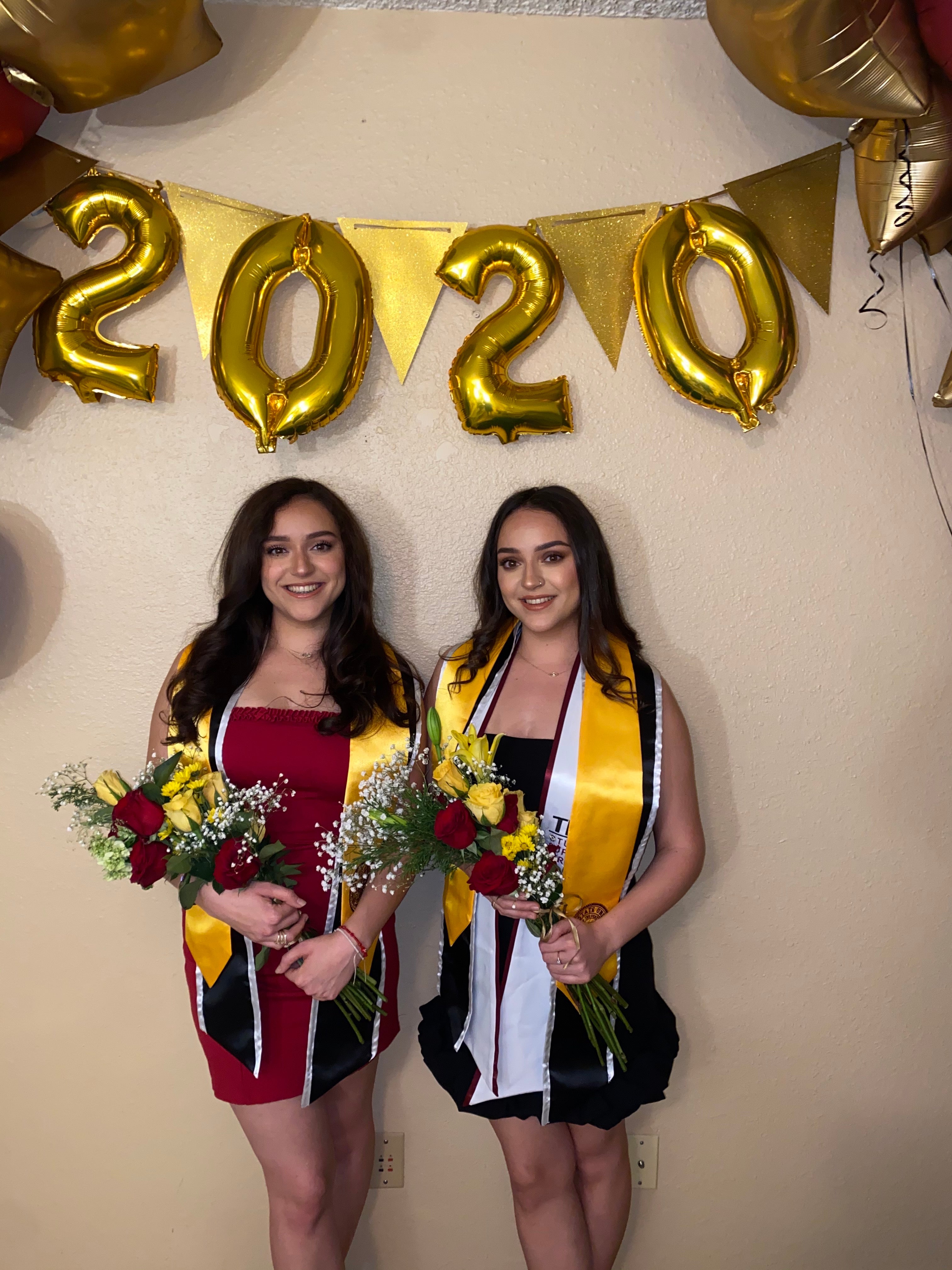 ASU twins Anahi and Sarahi Montano pose in front of graduation set up with balloons and flowers. 