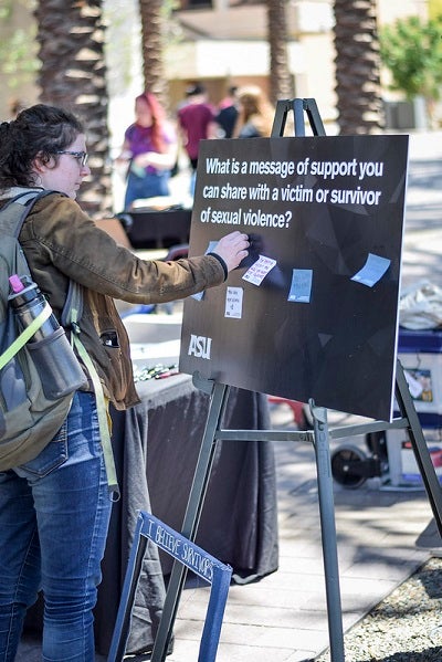 A student places a post-it on a sign that says "what is a message of support you an share with a victim or survivor of sexual violence?"