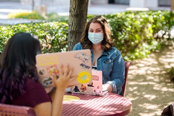 Two students in masks outside with laptops